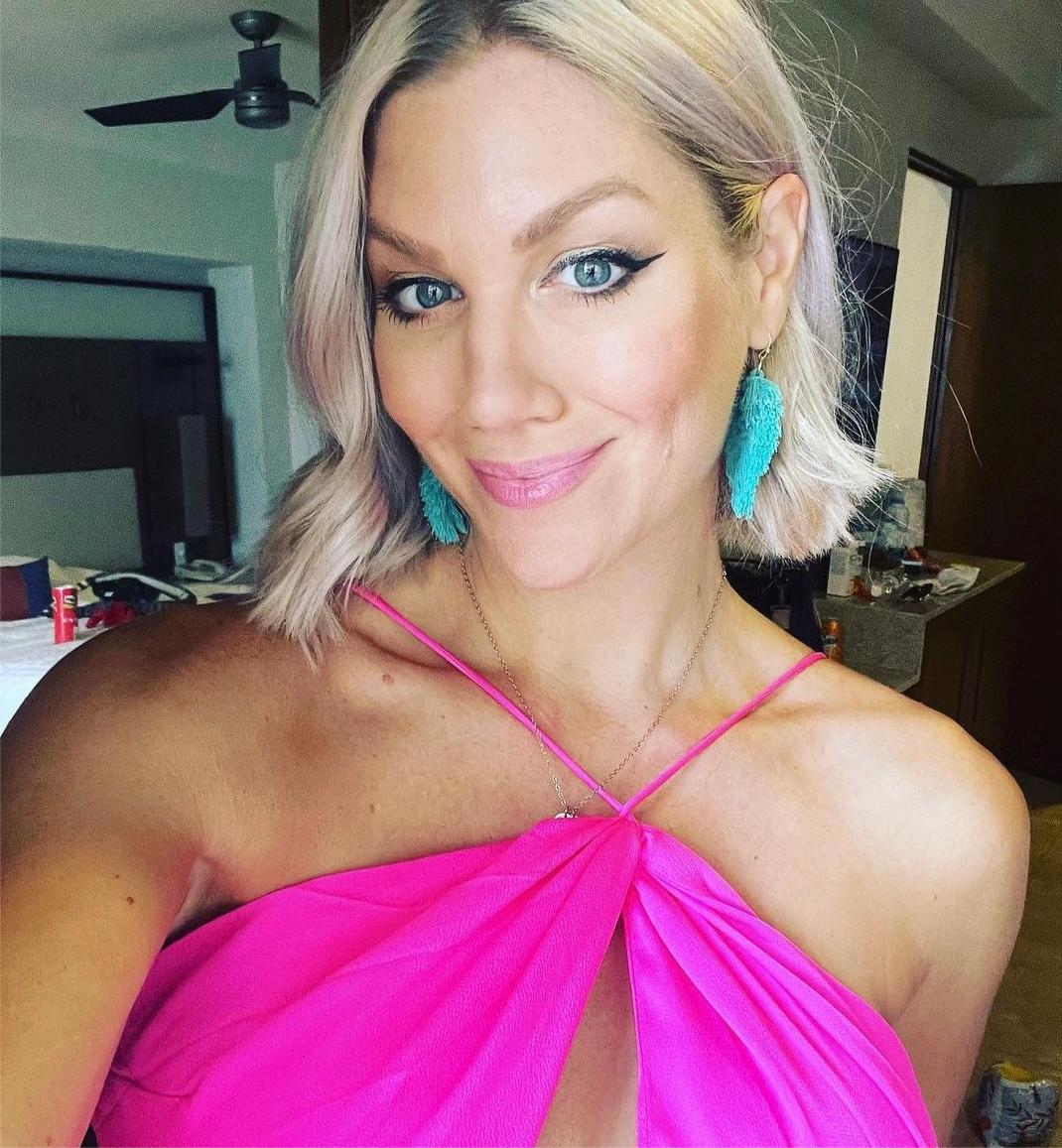 Woman wearing a bright pink top with blue earrings indoors.